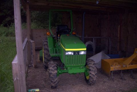 1984 Ford Bronco - A green tractor sits in a rustic wooden structure, with a yellow implement visible to the right.