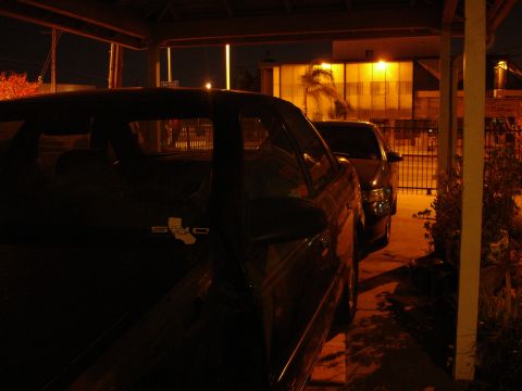 1993 Ford Taurus - Two cars are parked under a carport at night, with one car in the foreground and another behind it.