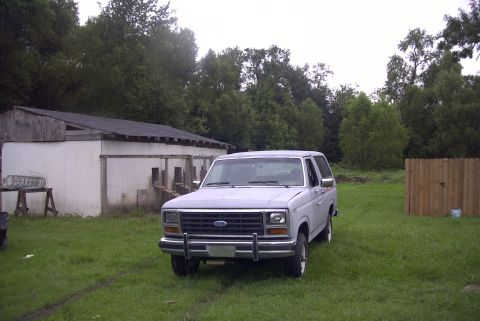 1984 Ford Bronco - This 1980s Ford Bronco is parked in front of a building with a wooden fence in the background.