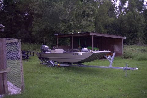 1984 Ford Bronco - A boat sits on a trailer in front of a shed, with trees in the background.