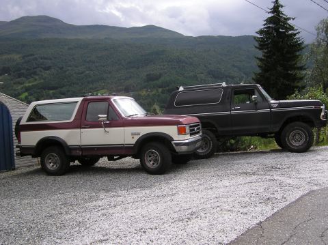 1978 Ford Bronco - Two Ford Broncos, one from 1978, are parked on a gravel lot with a mountainous backdrop.