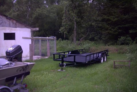 1984 Ford Bronco - A boat and trailer sit in a yard next to a building, with trees in the background.