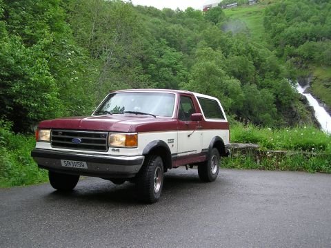 1989 Ford Bronco - This two-tone 1989 Ford Bronco is captured in a scenic setting with a waterfall cascading down a lush green hillside.