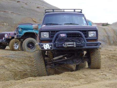 1986 Ford Bronco II - A dark brown Ford Bronco II is parked in the dirt with other off-road vehicles behind it.