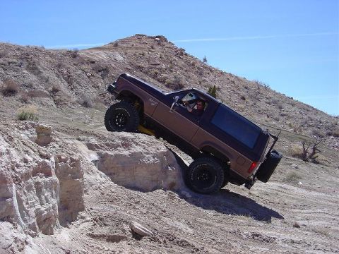 1986 Ford Bronco II - A brown 1986 Ford Bronco II navigates a steep, rocky off-road trail under a clear blue sky.