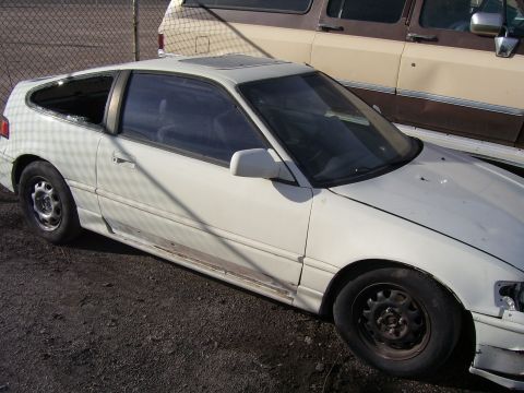 1993 Mazda MX-6 - A white Honda CRX is seen from a three-quarter front angle, showing damage to its rear window and side.