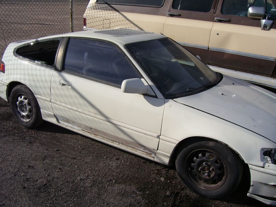 White Honda CRX with a broken rear window and dented side panel, parked outdoors