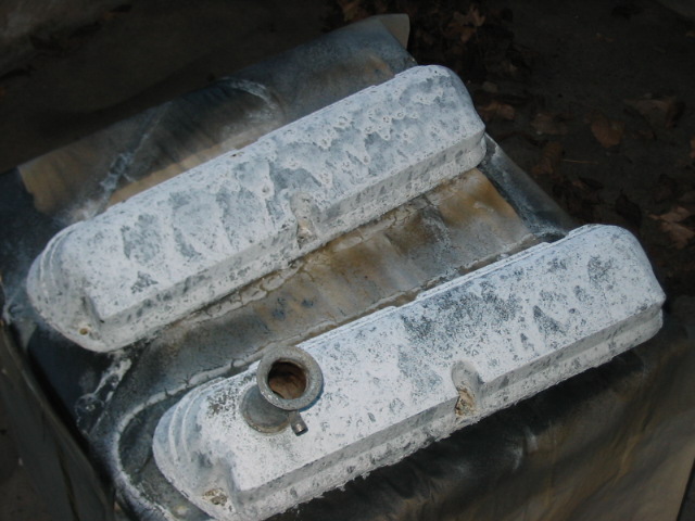 Two aluminum engine valve covers, coated in white residue, resting on a dark surface
