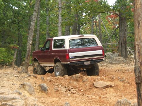 1993 Ford Bronco - Maroon and white Ford Bronco navigates a challenging off-road path.