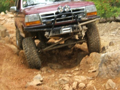 1993 Ford Bronco - This SUV is tackling a challenging off-road trail with large rocks and dirt.