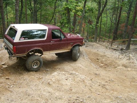 1993 Ford Bronco - 1993 Ford Bronco navigating a challenging off-road trail through a forest.