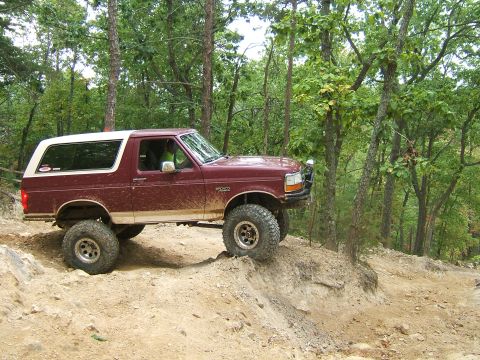 1993 Ford Bronco - A maroon Ford Bronco navigates a steep dirt path surrounded by trees.