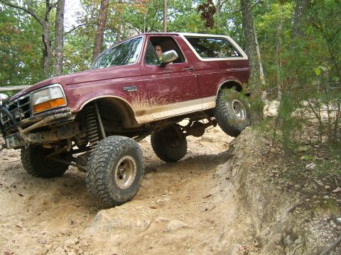 1993 Ford Bronco - 1993 Ford Bronco tackles a challenging off-road trail with one wheel off the ground.