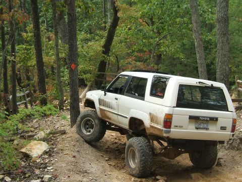 1993 Ford Bronco - A lifted Toyota 4Runner navigates a wooded trail with large off-road tires.