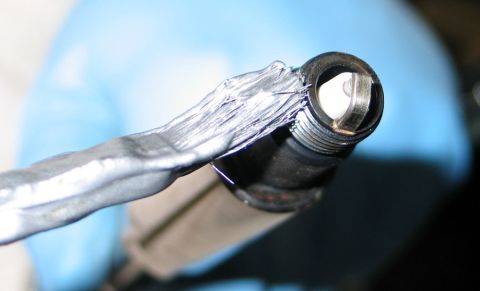 1994 Ford Bronco - A close-up view of a spark plug with damaged wiring, held by a gloved hand.