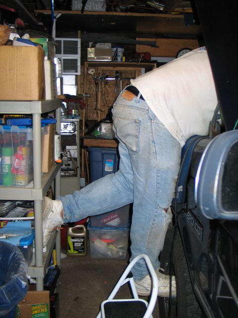 1994 Ford Bronco - A person is seen working on a vehicle in a cluttered garage.