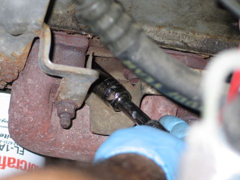 1994 Ford Bronco - Close-up of a socket wrench being used to remove a spark plug from a vehicle's engine manifold.