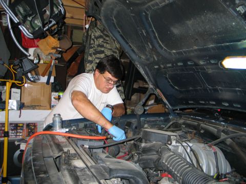 1994 Ford Bronco - A person is performing maintenance on the engine of a vehicle inside a cluttered garage.