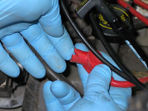 1994 Ford Bronco - Hands wearing blue gloves disconnect a red spark plug wire from an engine component.