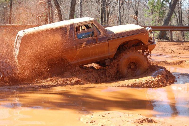 1978 Ford Bronco struggling through deep mud, throwing up spray