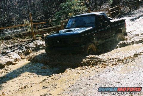 1993 Ford Bronco - A black 1993 Ford Bronco navigates a muddy trail, with its tires deep in the mire.
