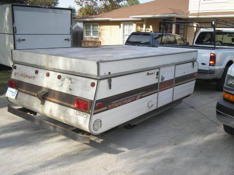 1966 Ford Bronco - A Starcraft pop-up camper trailer is parked in a driveway, with two pickup trucks visible behind it.