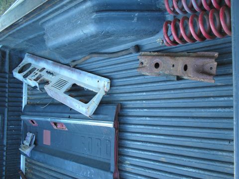 1966 Ford Bronco - Salvaged parts laid out in a black ribbed pickup bed liner: a bare metal early Bronco dash panel with gauge cutouts and defroster vents, a…