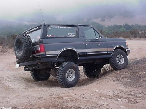 1988 Ford Bronco - Modified Ford Bronco navigates a dirt trail with large off-road tires.