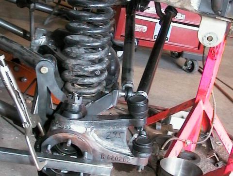 1995 Ford Bronco - Front axle assembly on a shop floor with a coil spring, radius arm, tie rod ends and drag link fitted, and the wheel hub area disassembled.…