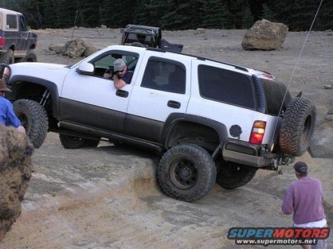 1990 Ford Bronco - White SUV with aftermarket bumper and spare tire on rear is off-roading on a dirt trail.