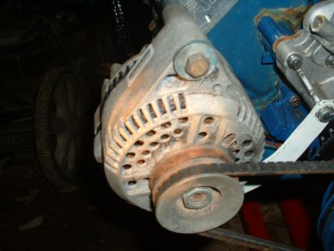 1985 Ford Bronco - Close-up of an alternator, pulley, and drive belt attached to a blue engine block.