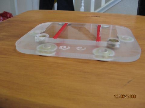 1994 Ford Bronco - A clear plastic component with red accents and decorative swirls is shown on a wooden surface.