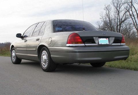 2001 Ford Crown Victoria - The rear of a gray 2001 Ford Crown Victoria sedan is shown from a low angle on a paved road.