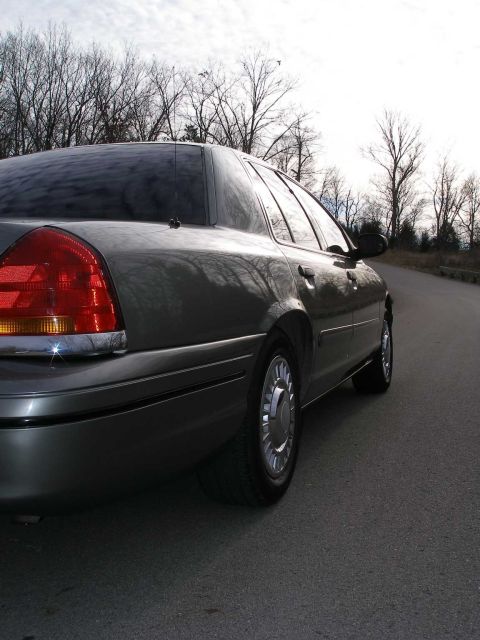 2001 Ford Crown Victoria - Rear view of a 2001 Ford Crown Victoria parked on the side of a road with trees in the background.