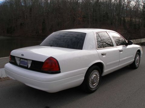 2001 Ford Crown Victoria - A white 2001 Ford Crown Victoria sedan is viewed from the rear three-quarter angle, parked outdoors.