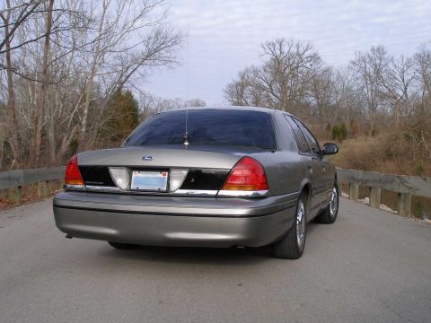 2001 Ford Crown Victoria - A gray 2001 Ford Crown Victoria is parked on a road with trees in the background.