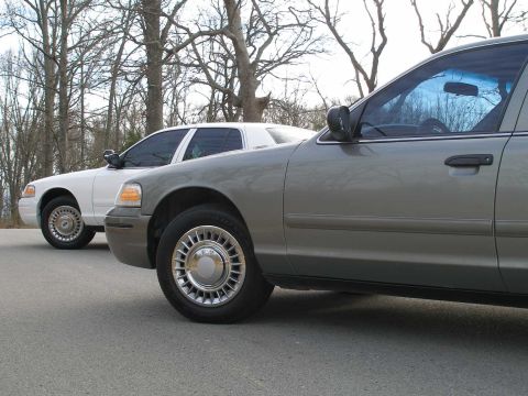 2001 Ford Crown Victoria - Two Ford Crown Victorias, a gray one in the foreground and a white one behind it, are parked outdoors.