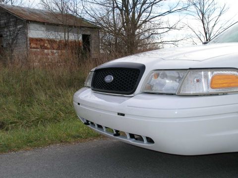 2001 Ford Crown Victoria - A white Ford Crown Victoria is parked on the side of a road, with an abandoned shed in the background.