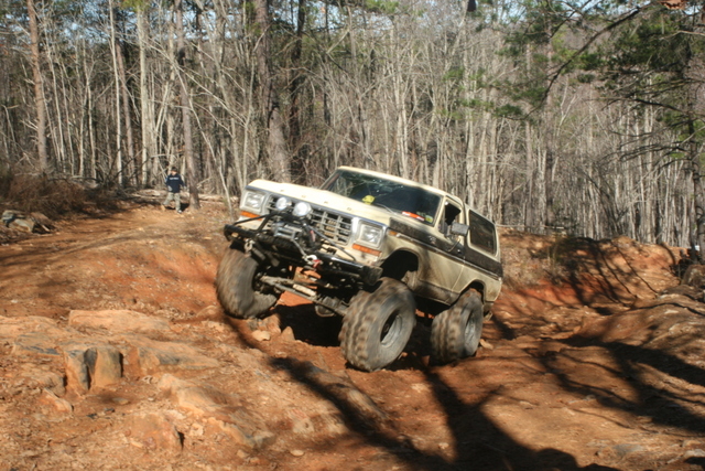 Off-road Bronco climbing a dirt hill with trees in the background