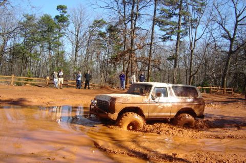 1992 Ford Mustang - A muddy Ford Bronco navigates a challenging off-road course, with onlookers observing the action.