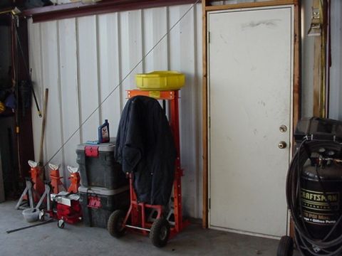 1988 Ford Bronco - A cluttered garage scene features various tools, storage bins, and a large object covered by a dark tarp on a wheeled stand.