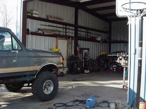 1988 Ford Bronco - A gray Ford Bronco with a tan stripe is parked inside a metal garage with various tools and equipment.