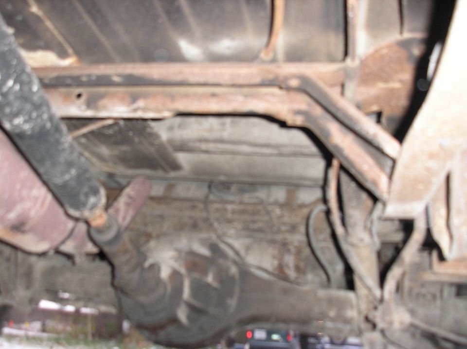 Underside of a rusty vehicle with visible suspension components and exhaust system