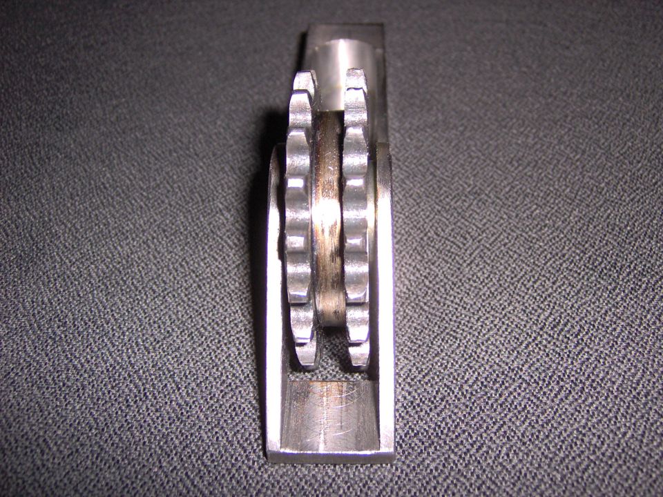 Machined metal sprocket and roller mounted in an aluminum bracket on gray fabric