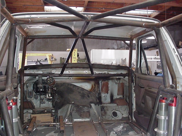 Gutted SUV interior with bare-metal roll cage and stripped rusty firewall in a garage