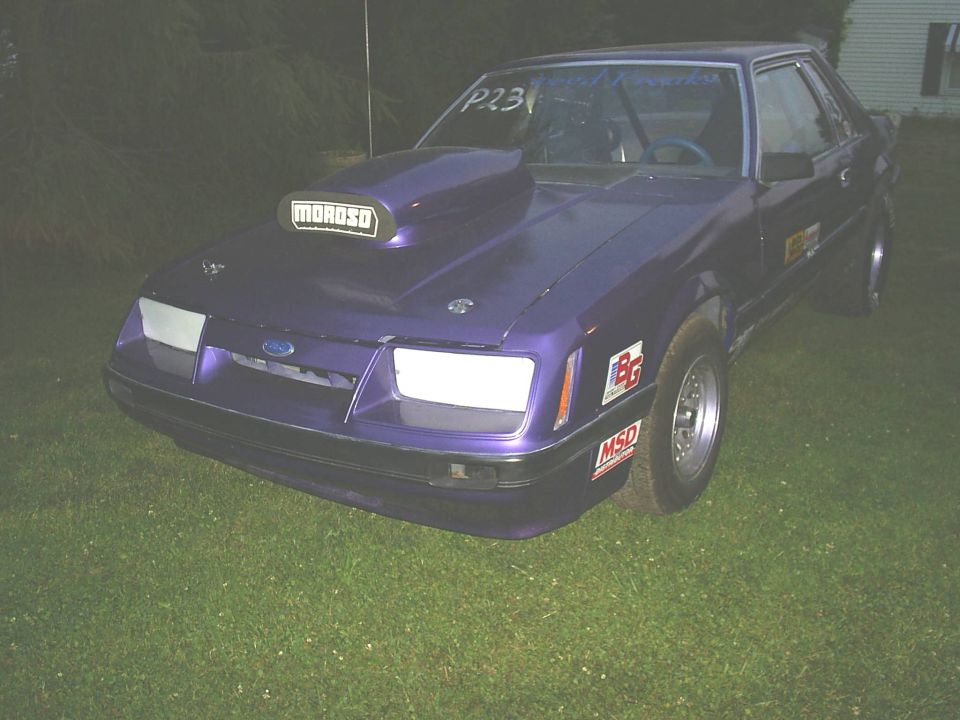 Purple 1985 Ford Mustang drag car with a large hood scoop and racing decals