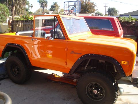 1977 Ford Bronco - Orange 1977 Ford Bronco with a basketball hoop on the roof, parked next to a red SUV.