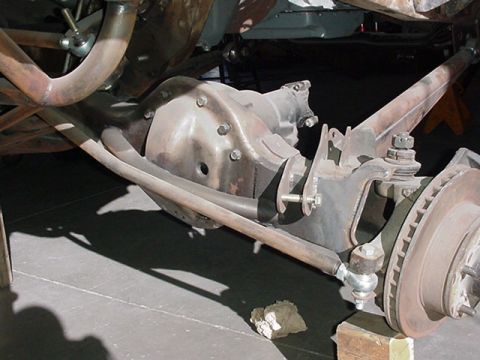 1988 Ford Bronco - Underside view of a front differential/axle assembly with a cast pumpkin housing, tie rod, coil spring, and a brake rotor visible at right.…