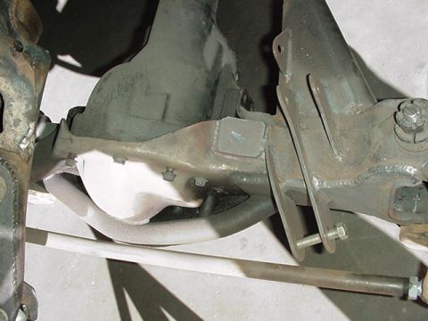 1988 Ford Bronco - Close-up underside view of a front suspension showing a cast differential housing, a painted axle beam, radius arm bracket with U-bolts, an…