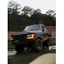 1993 Ford Bronco - This lifted Ford Bronco is shown off-road, navigating through a muddy area with trees in the background.